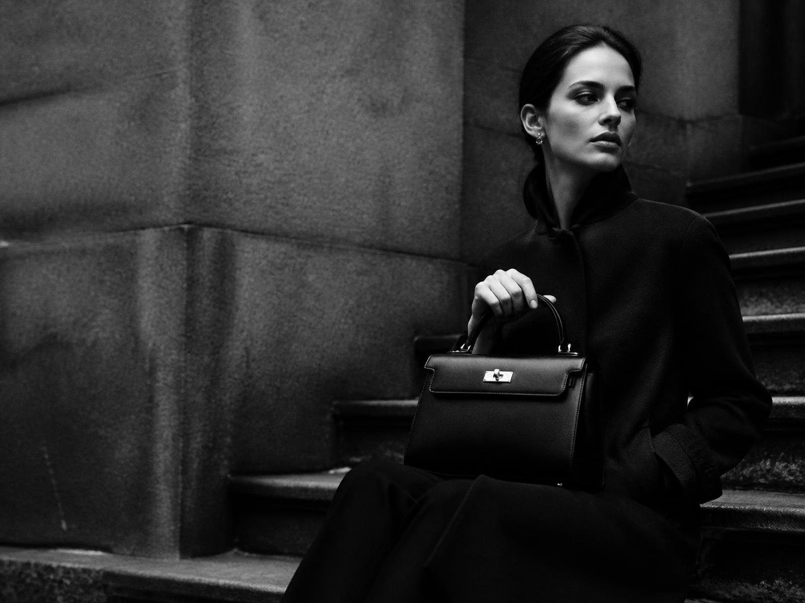 Black and white editorial portrait of a woman holding a structured luxury handbag